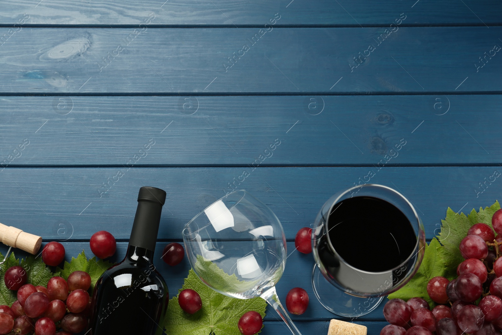 Photo of Tasty red wine and grapes on blue wooden table, flat lay. Space for text