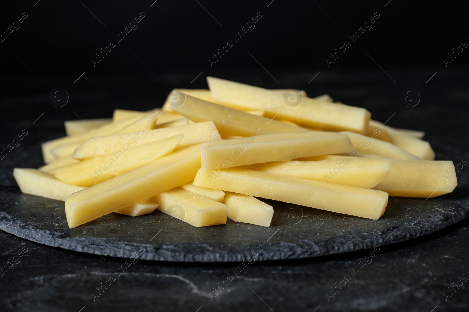 Photo of Cut raw potatoes on black table, closeup