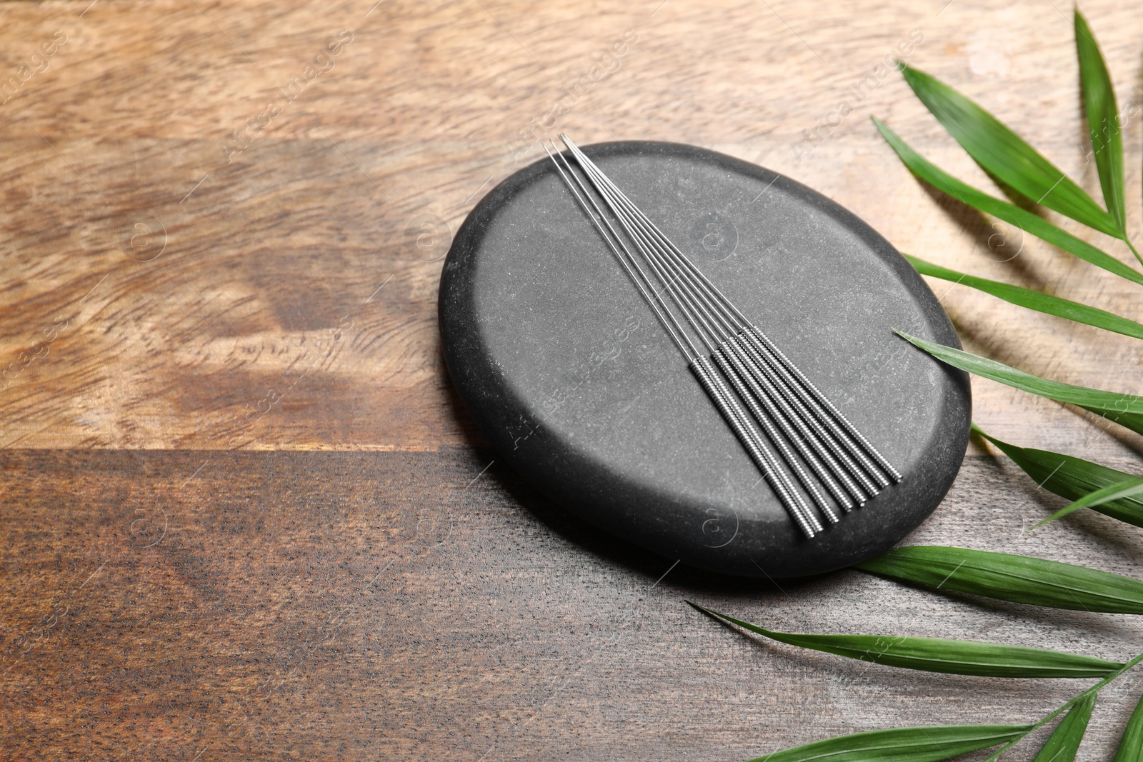 Photo of Acupuncture needles, spa stone and leaf on wooden table, above view. Space for text