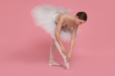 Photo of Young ballerina practicing dance moves on pink background