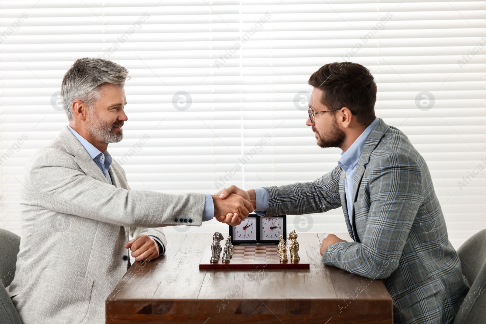 Photo of Men shaking their hands during chess tournament at table indoors