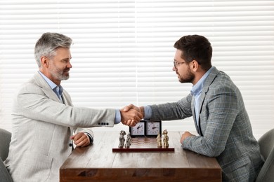Men shaking their hands during chess tournament at table indoors