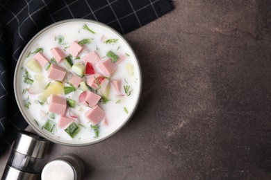 Delicious cold summer soup (okroshka) with boiled sausage in bowl on brown table, top view. Space for text