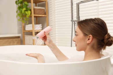 Woman pouring shower gel onto hand in bath indoors