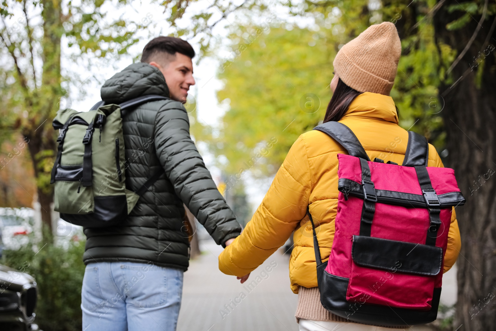 Photo of Couple with travel backpacks on city street, back view. Urban trip