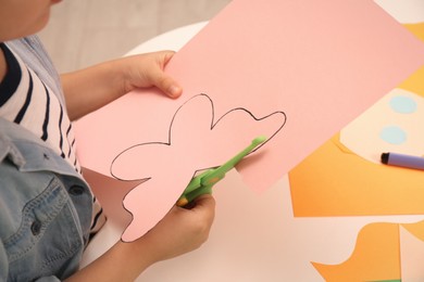 Photo of Little boy cutting color paper with scissors at table indoors, closeup