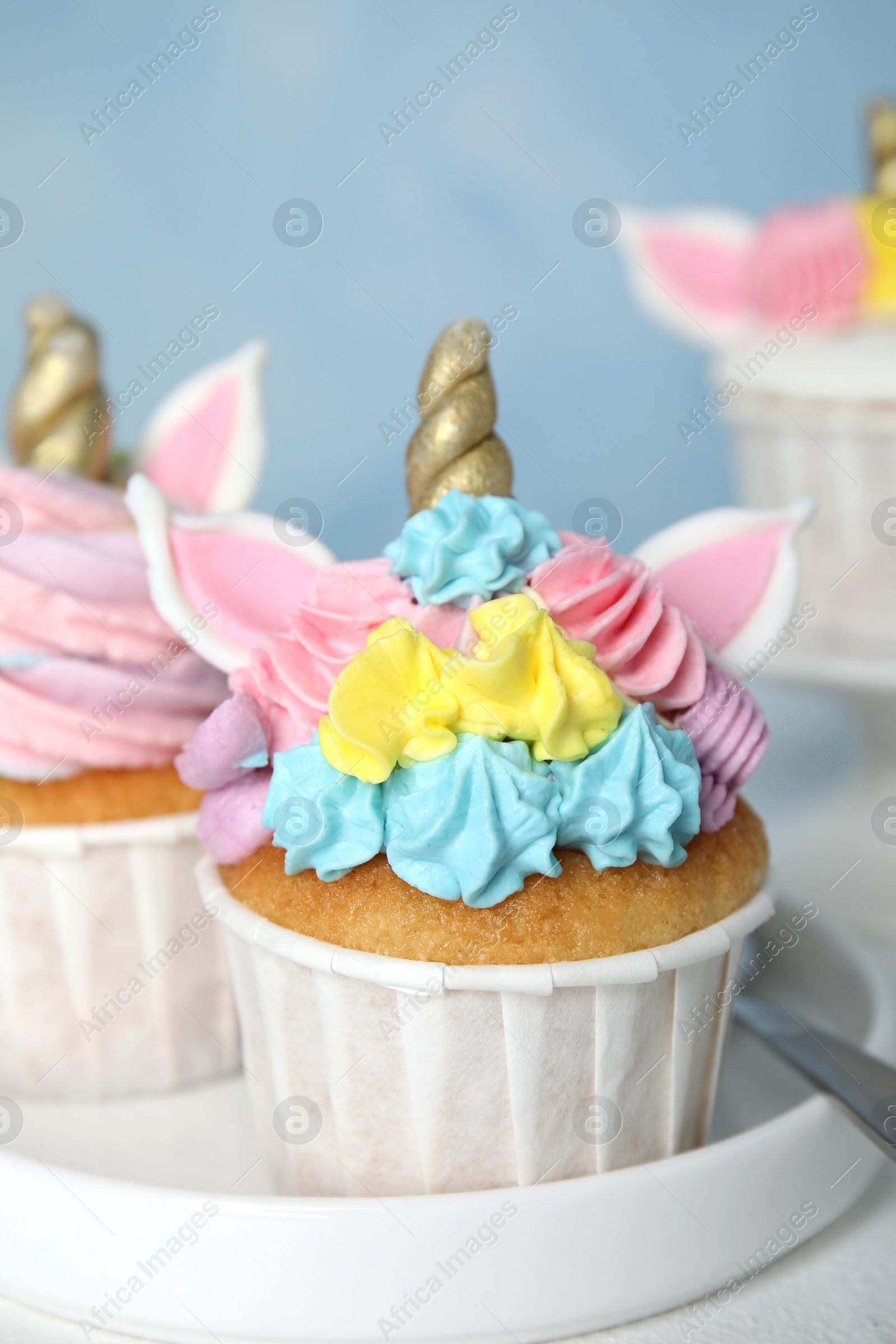 Photo of Plate with two cute sweet unicorn cupcakes on white table, closeup