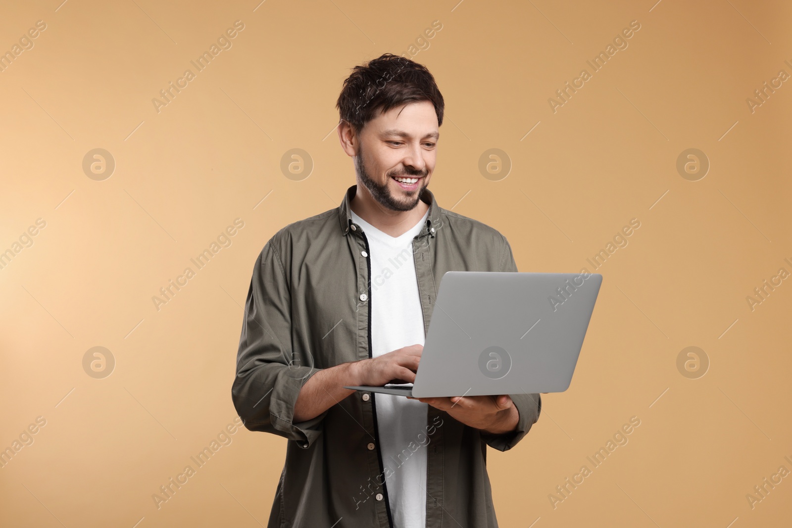 Photo of Happy man with laptop on beige background