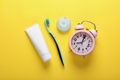Container with dental floss, toothpaste and toothbrush on yellow background, flat lay