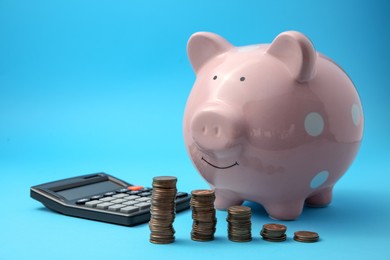 Photo of Piggy bank, stacks of coins and calculator on light blue background