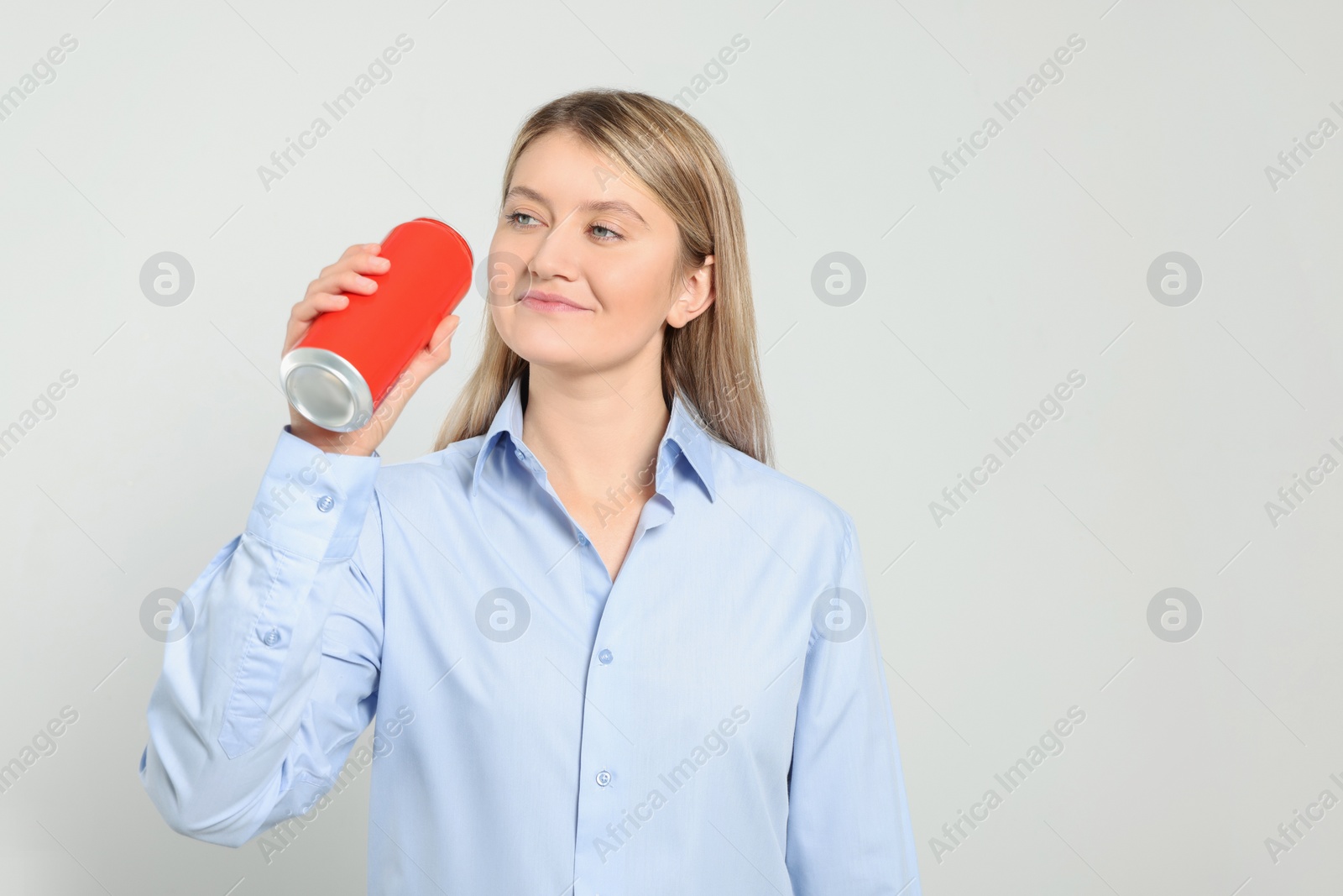 Photo of Beautiful happy woman holding red beverage can on light background. Space for text