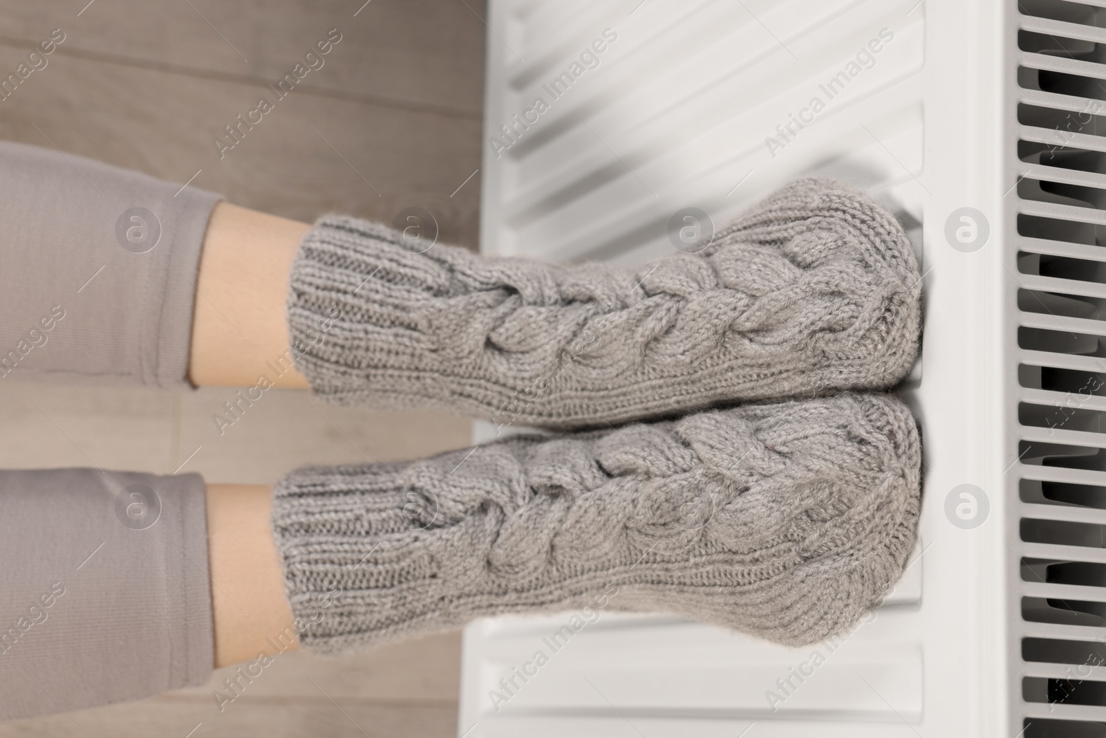 Photo of Woman warming feet near heating radiator, above view