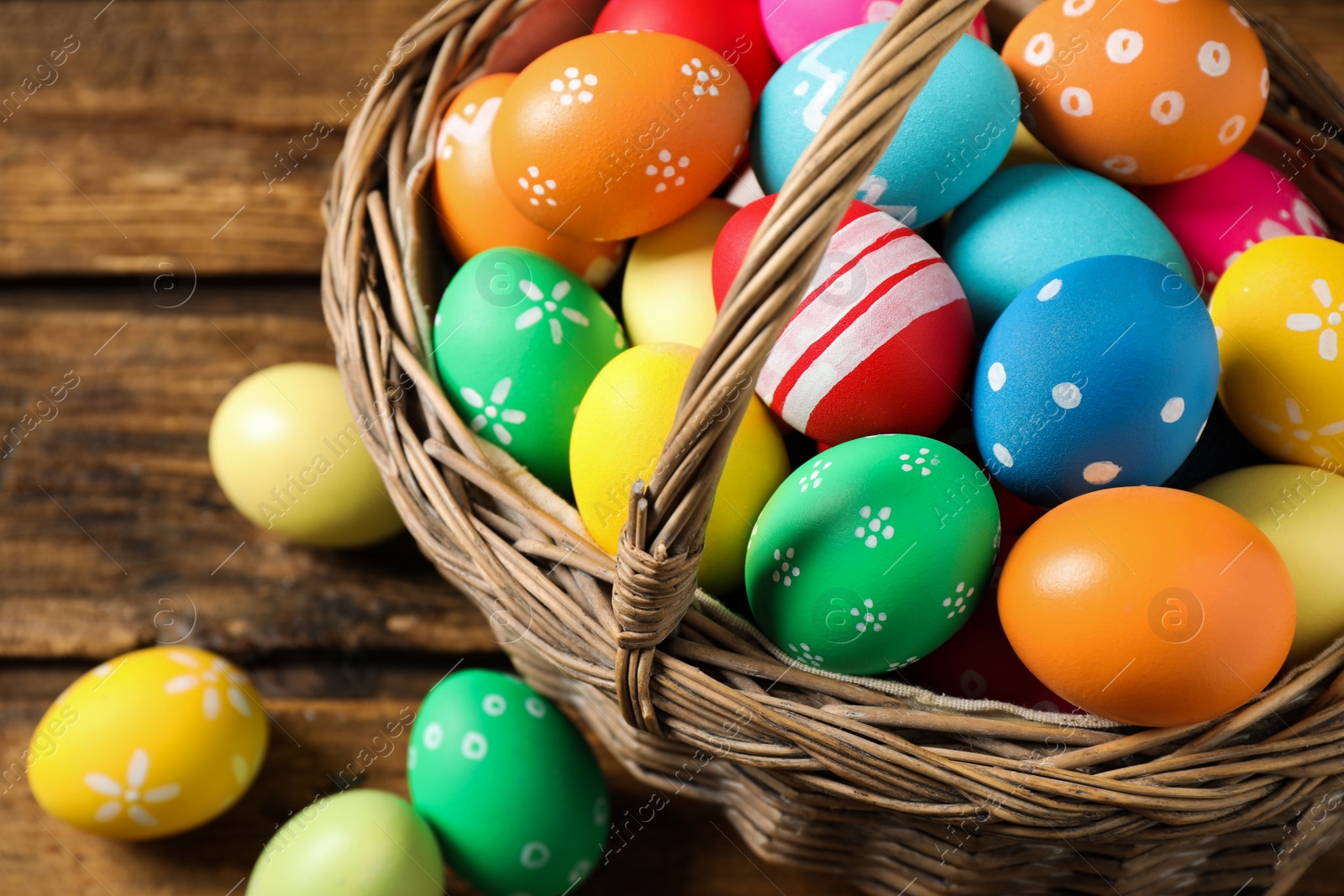 Photo of Colorful Easter eggs in basket on wooden background, closeup