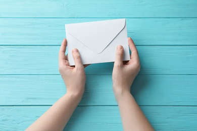 Photo of Woman with white paper envelope at light blue wooden table, top view