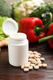 Photo of Dietary supplements. Plastic bottle, pills and food products on wooden table