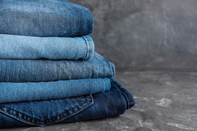 Photo of Stack of different jeans on grey table, closeup. Space for text