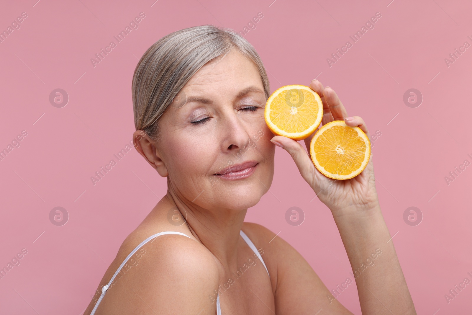 Photo of Beautiful woman with halves of orange rich in vitamin C on pink background