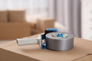 Photo of Dispenser with roll of adhesive tape on box indoors, closeup