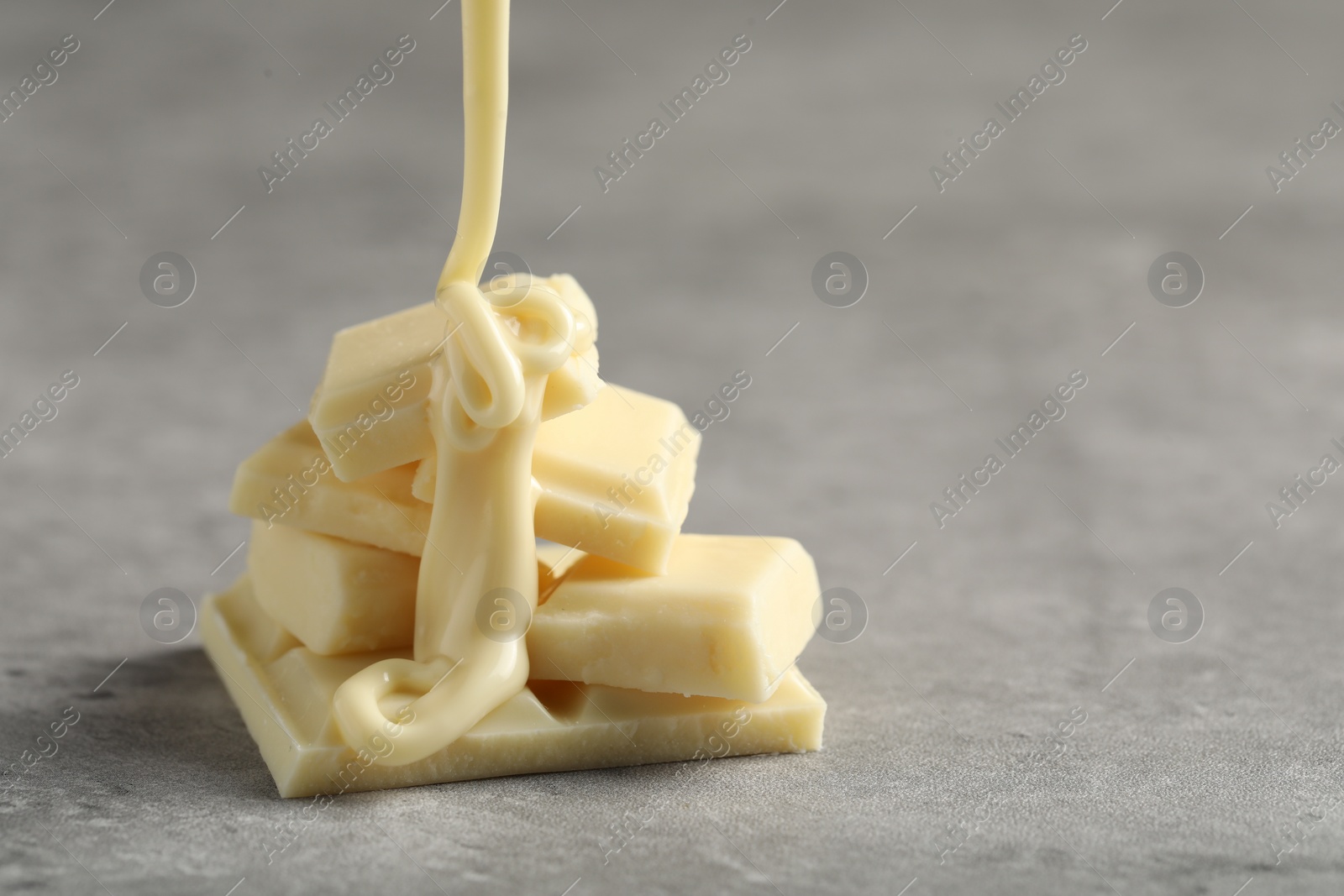 Photo of Pouring tasty white chocolate paste onto pieces on grey table, closeup. Space for text