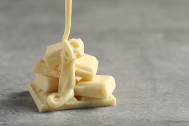 Pouring tasty white chocolate paste onto pieces on grey table, closeup. Space for text