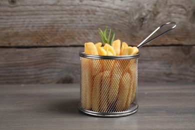 Photo of Delicious French fries in metal basket on wooden table