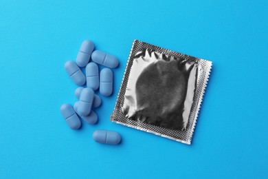 Photo of Pills and condom on light blue background, flat lay. Potency problem