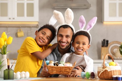 Photo of Happy African American father and his cute children with Easter eggs at table in kitchen