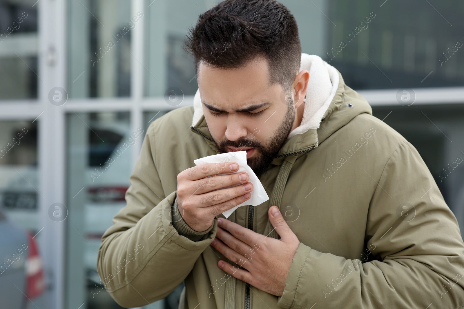 Photo of Sick man with tissue coughing outdoors. Cold symptoms