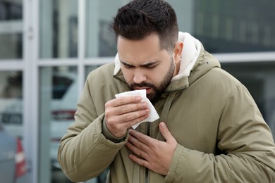 Photo of Sick man with tissue coughing outdoors. Cold symptoms