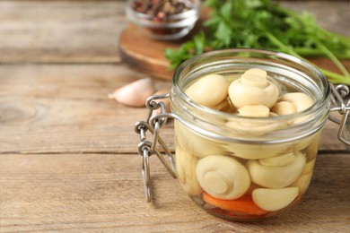 Photo of Jar with marinated mushrooms on wooden table, closeup. Space for text