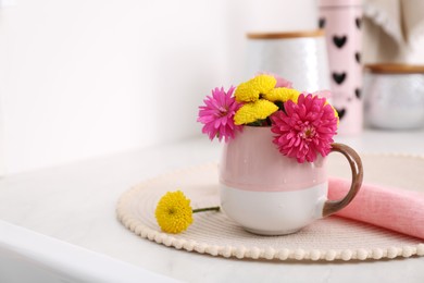 Beautiful bright flowers in cup on table indoors, space for text