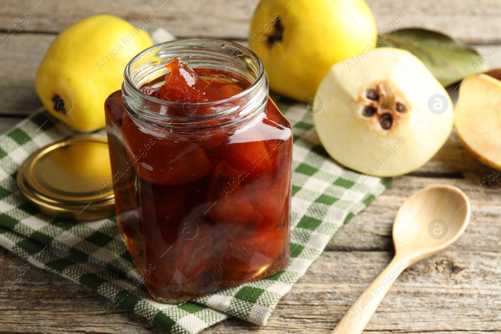 Photo of Tasty homemade quince jam in jar, spoon and fruits on wooden table, closeup