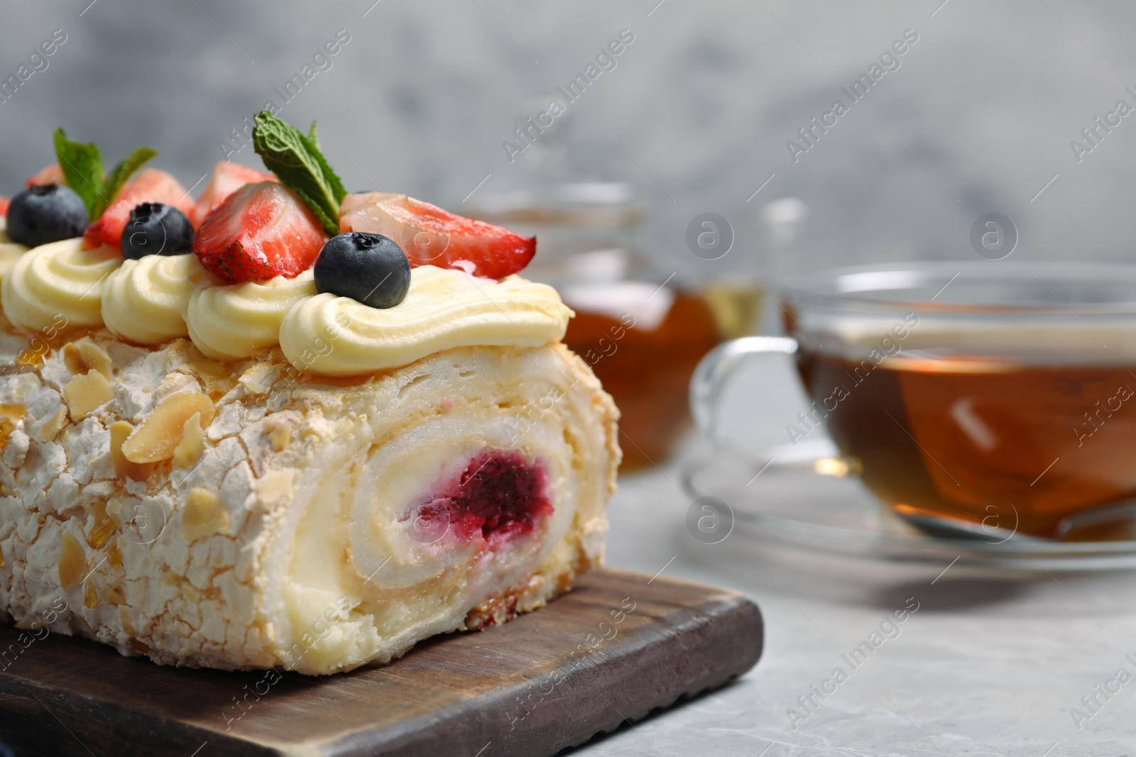 Photo of Tasty meringue roll with jam, cream, strawberry, blueberry and mint on light grey table, closeup. Space for text