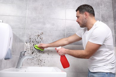 Image of Man using mold remover and brush on wall in bathroom