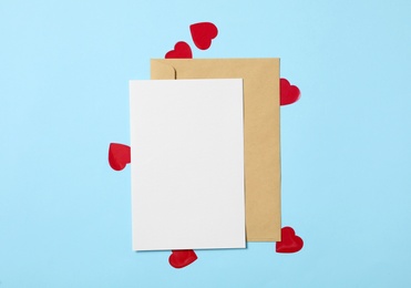 Blank card and paper hearts on light blue background, flat lay with space for text. Valentine's Day celebration