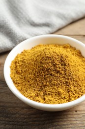 Photo of Dry curry powder in bowl on wooden table, closeup