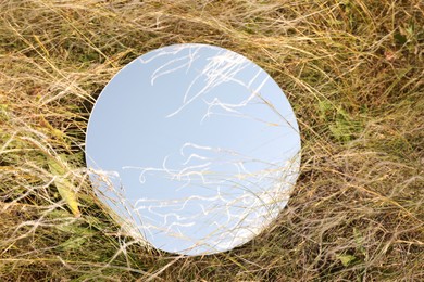 Photo of Spring atmosphere. Round mirror among grass and spikelets on sunny day