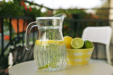Photo of Jug with refreshing lemon water and citrus fruits in bowl on light table outdoors