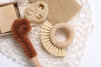 Cleaning brushes, sponge, loofah and soap bar on white table, top view