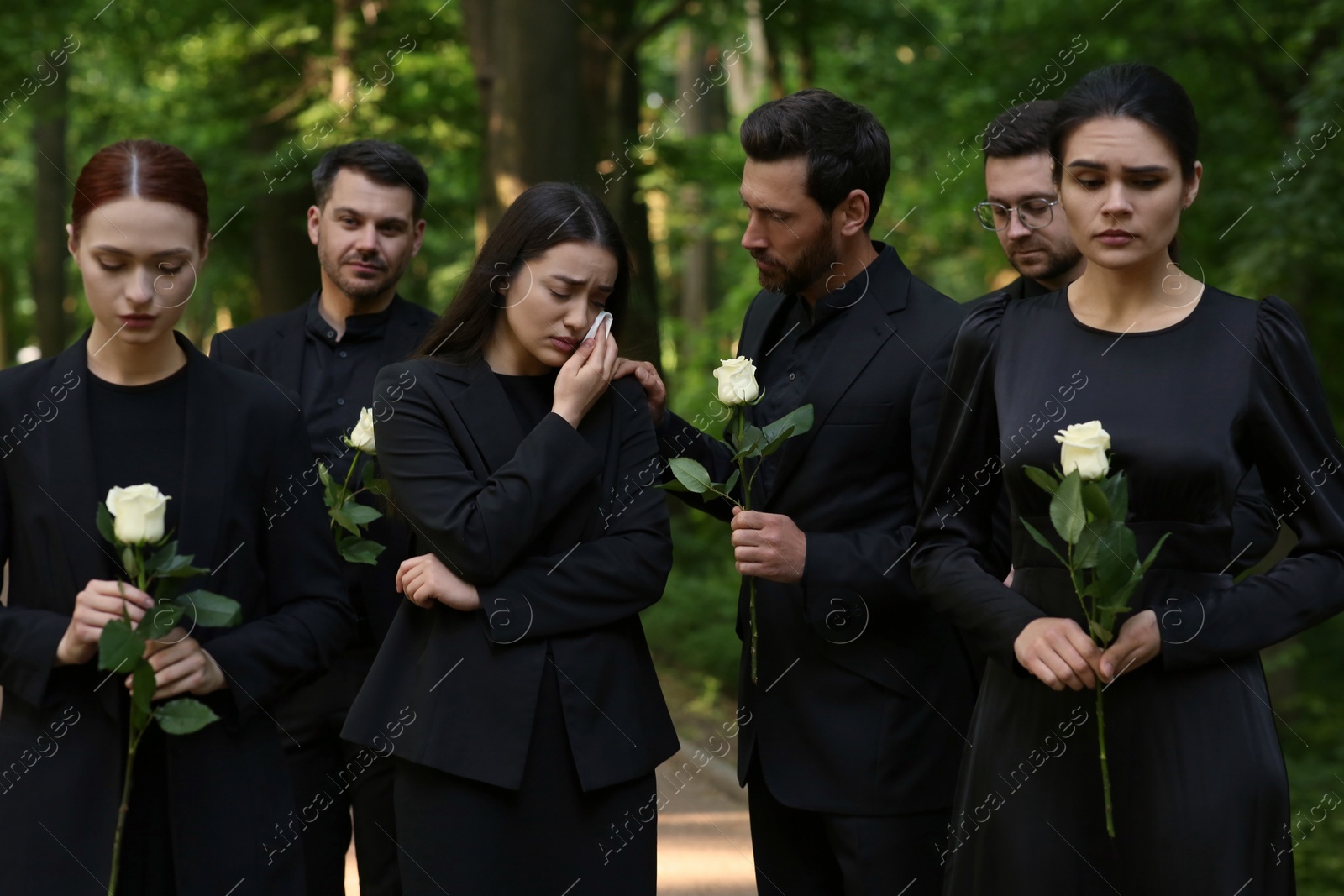 Photo of Funeral ceremony. Sad people with white rose flowers mourning outdoors