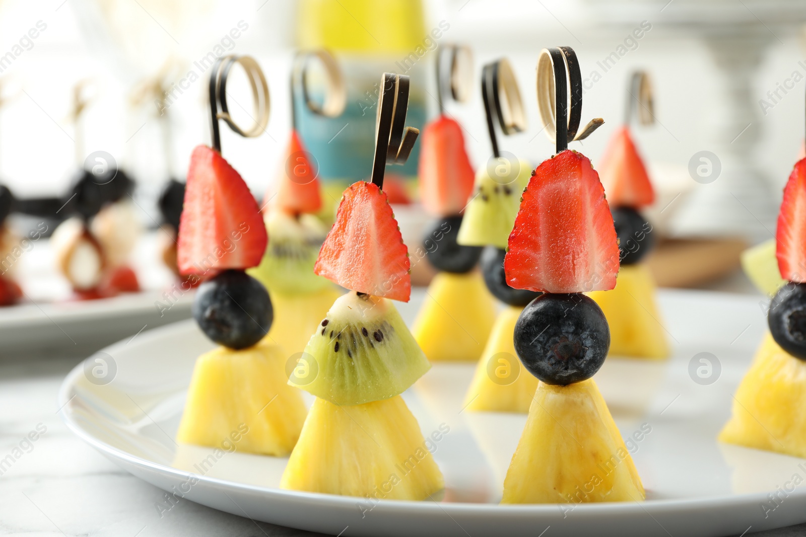 Photo of Tasty canapes with pineapple, kiwi and berries on white marble table, closeup