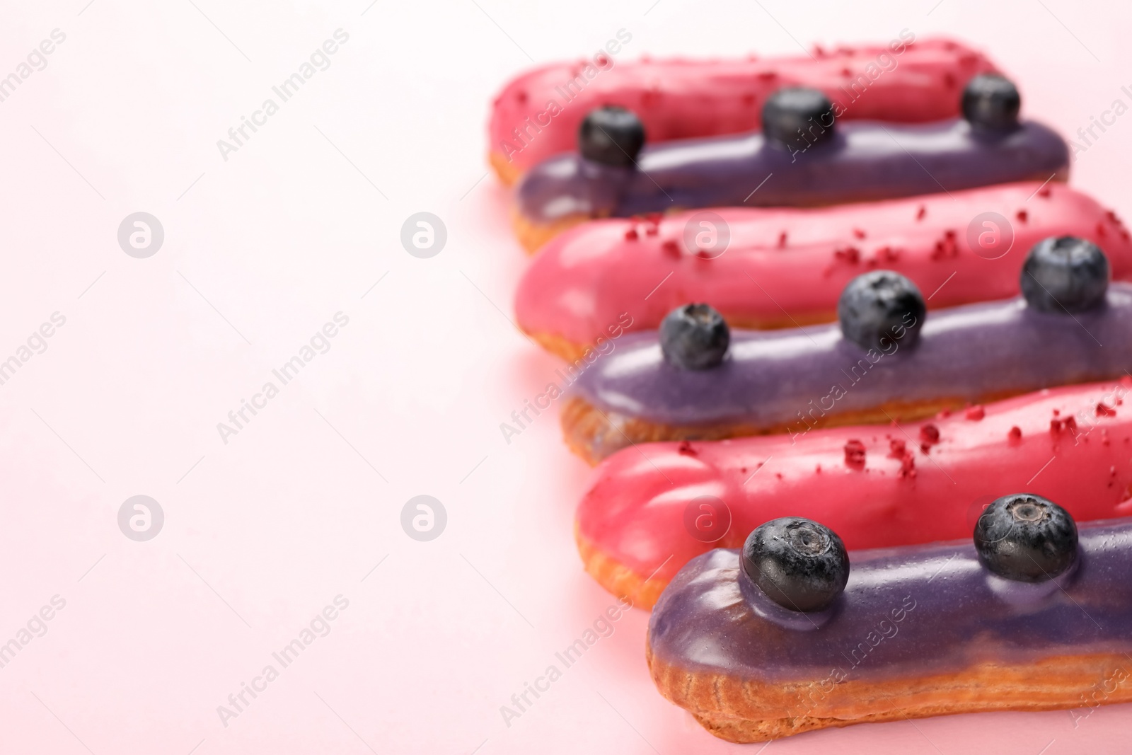 Photo of Delicious eclairs covered with glaze on pink background, closeup. Space for text