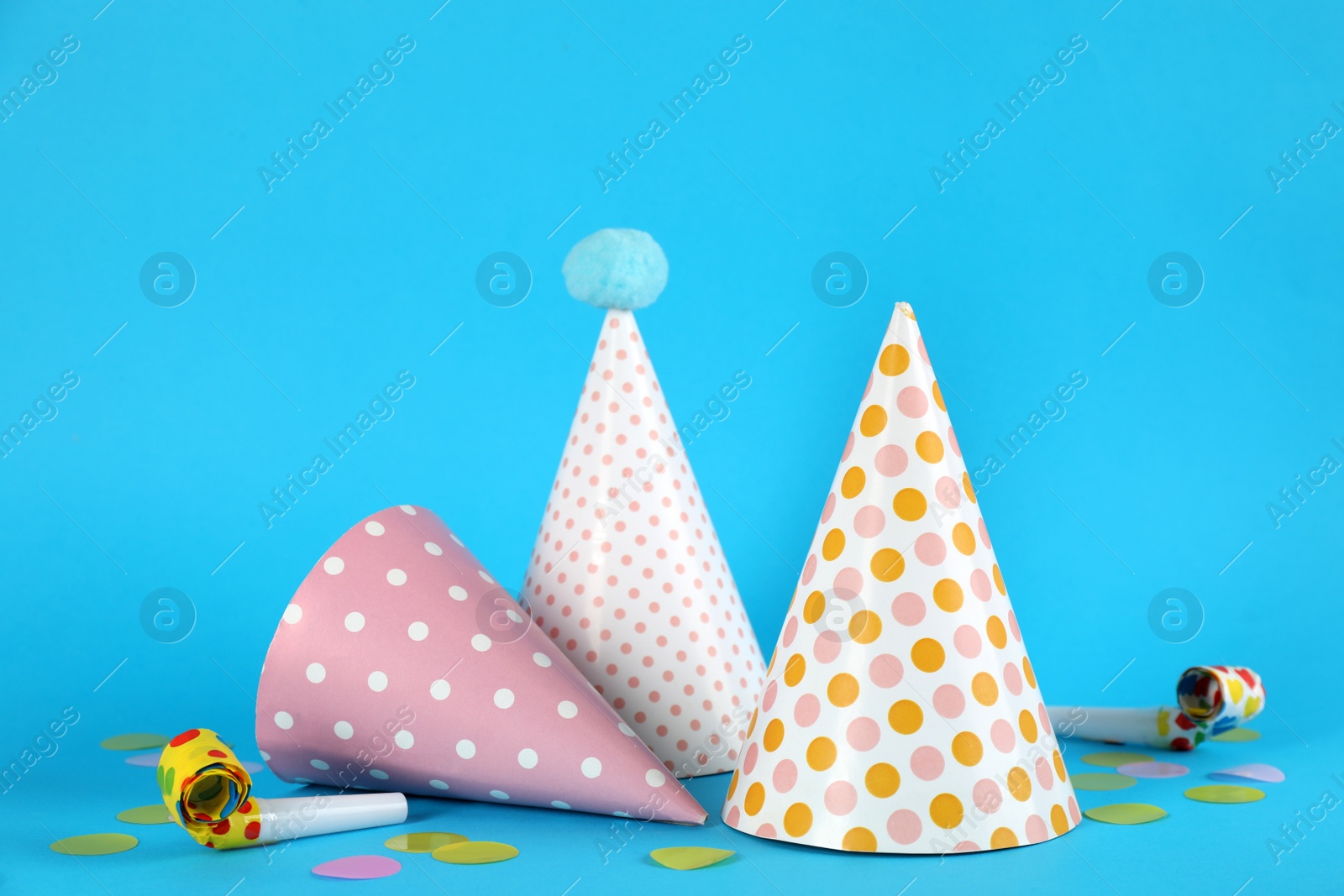 Photo of Bright party hats, horns and confetti on light blue background