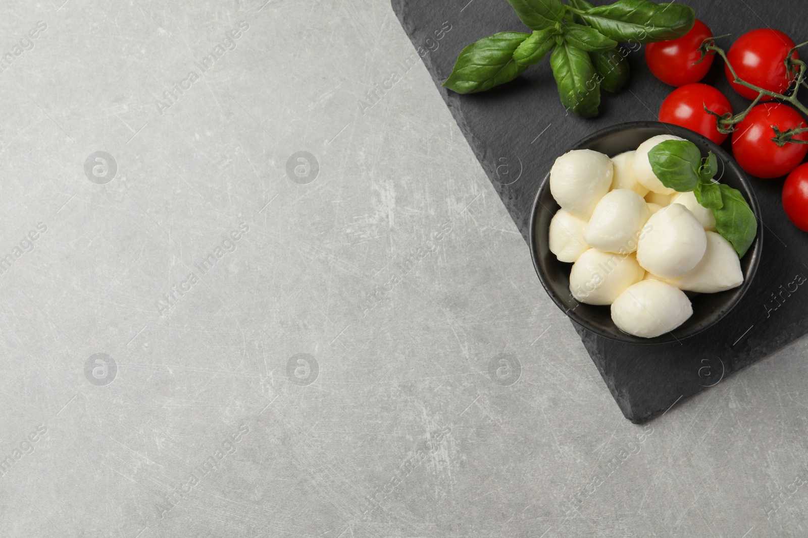 Photo of Delicious mozzarella balls, basil and tomatoes on light gray table, flat lay. Space for text