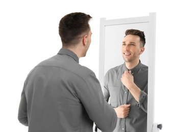 Photo of Young man looking at himself in mirror on white background