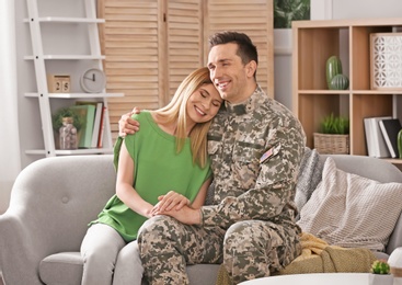 Photo of Young man in military uniform with his wife on sofa at home