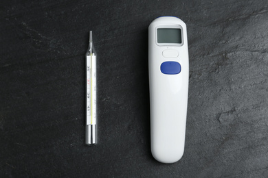Photo of Non-contact infrared and mercury thermometers on black slate background, flat lay