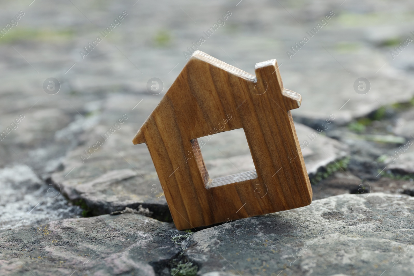 Photo of Wooden house model between cracks on stone road. Earthquake disaster