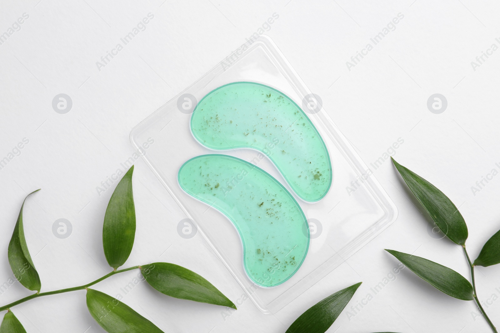 Photo of Package with under eye patches and green twigs on white background, flat lay. Cosmetic product