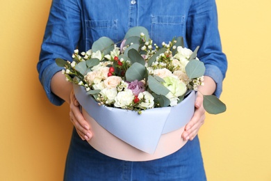 Female florist holding box with flowers on color background